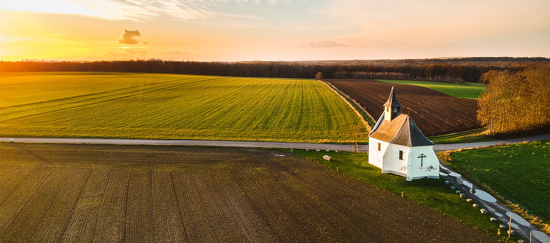 Photo d'une chapelle dans les champs avec un coucher du soleil